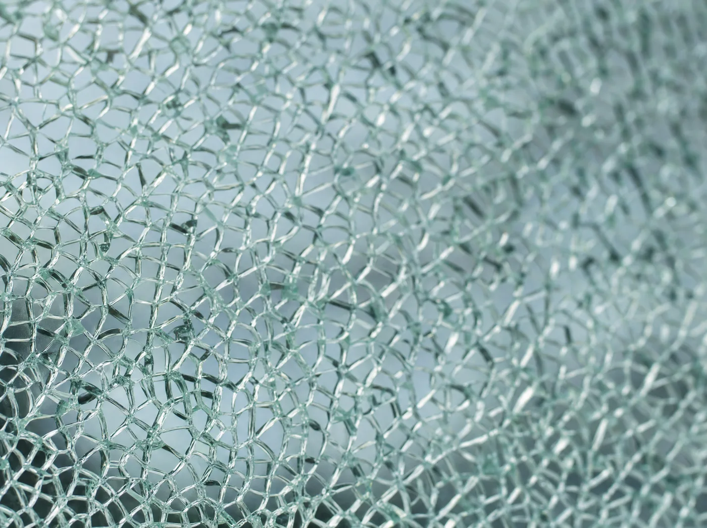 Tempered glass shattered into a crack web, held flat by clear safety film